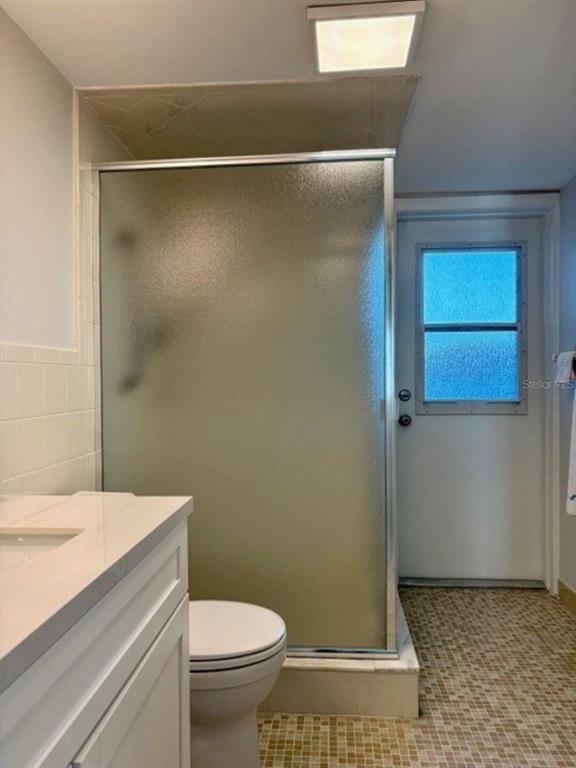 A bathroom features a glass-enclosed shower, a white vanity, a toilet, and a tiled floor — 815 OCEAN SHORE BOULEVARD UNIT 13, ORMOND BEACH, FL
