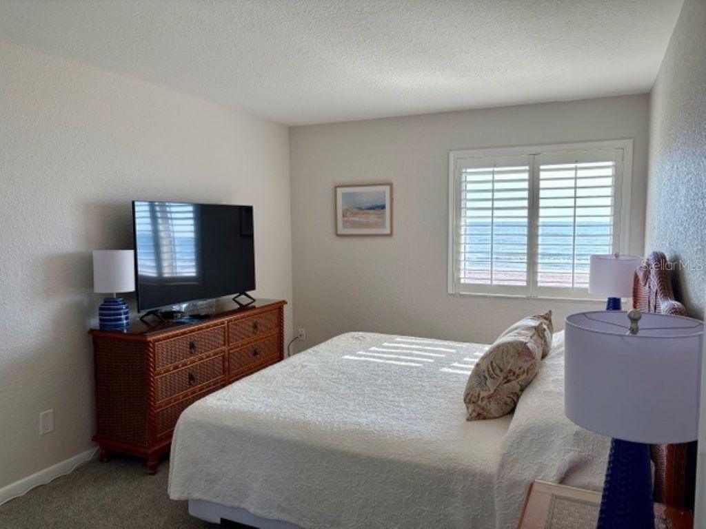 A bedroom features a bed, a wicker dresser with a television, and a window with shutters — 815 OCEAN SHORE BOULEVARD UNIT 13, ORMOND BEACH, FL