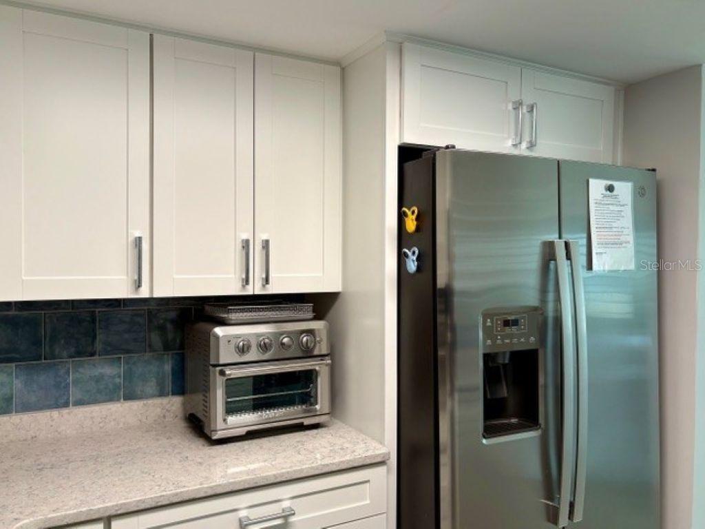 A kitchen features white shaker cabinets, a stainless steel refrigerator, and a blue tiled backsplash — 815 OCEAN SHORE BOULEVARD UNIT 13, ORMOND BEACH, FL