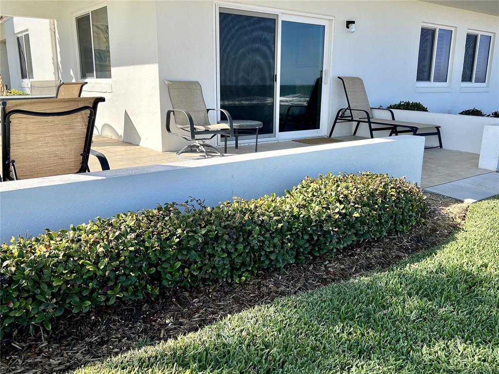 A patio with outdoor furniture sits in front of a white building with sliding doors — 815 OCEAN SHORE BOULEVARD UNIT 13, ORMOND BEACH, FL