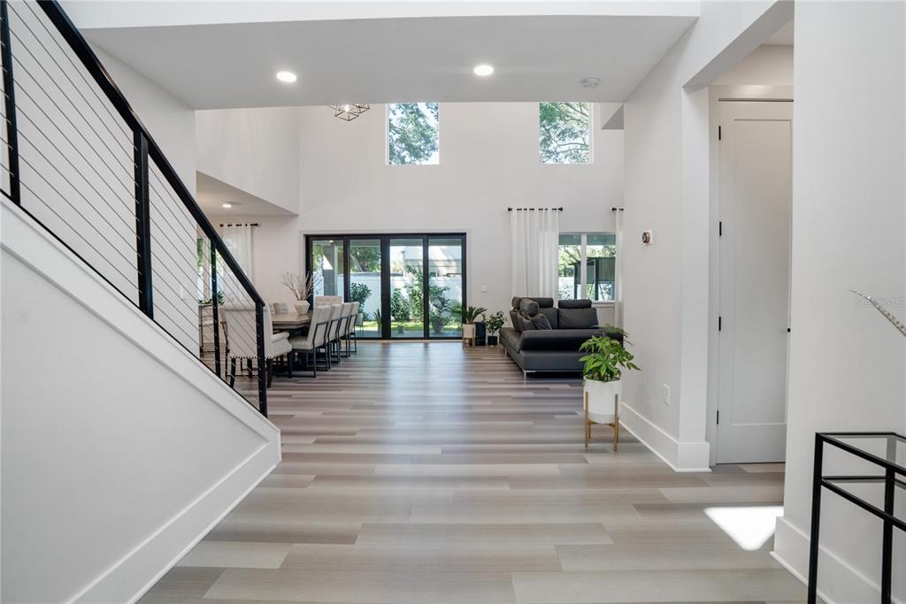 A bright, open-concept living and dining area features light wood-look flooring and a modern staircase — 2140 CATALINA DRIVE, CLEARWATER, FL