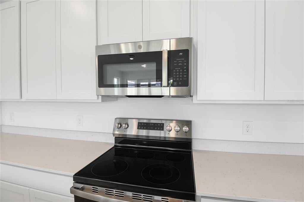 A stainless steel microwave is mounted above a black electric range in a white kitchen — 816 LAKE DELL ROAD, DUNDEE, FL