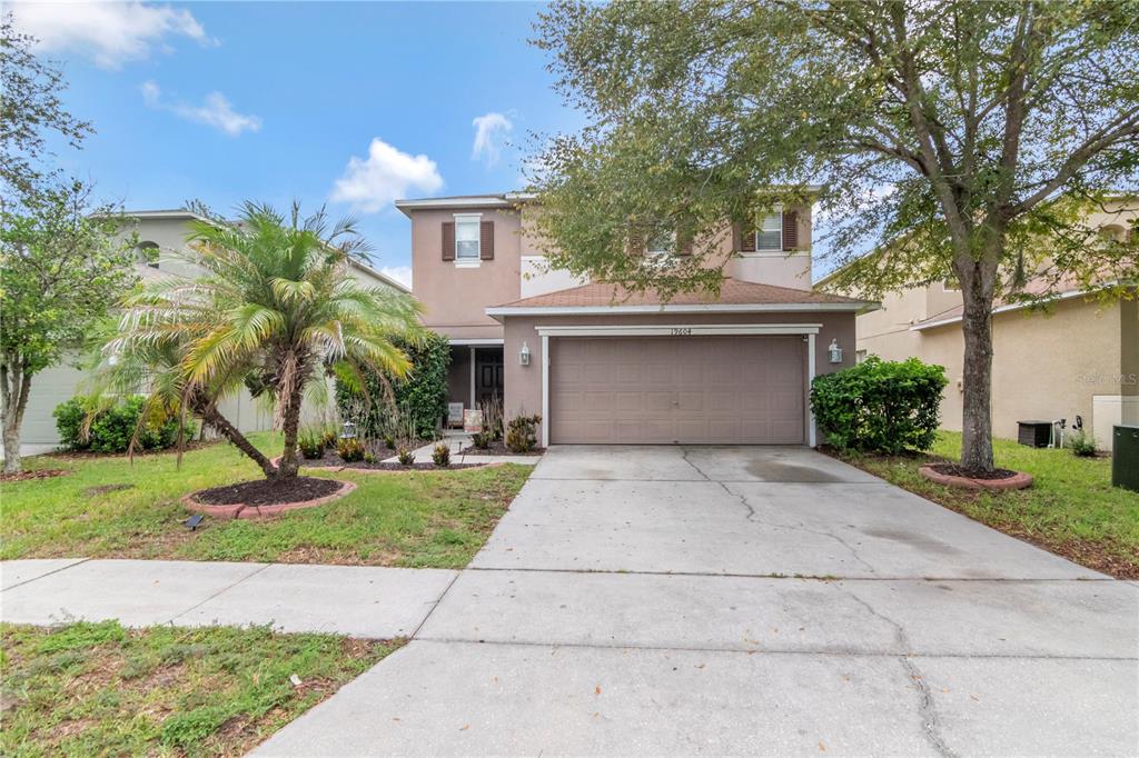 A two-story suburban house features a two-car garage, a palm tree, and a concrete driveway — 19604 TIMBERBLUFF DRIVE, LAND O LAKES, FL