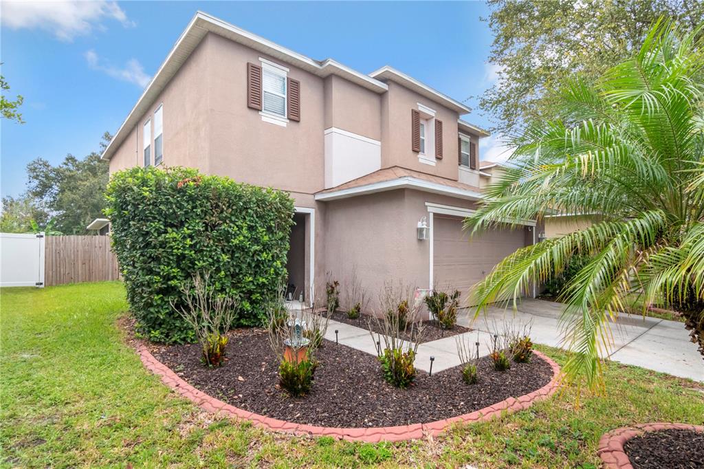 A two-story tan house with a garage, a front garden bed, and a palm tree — 19604 TIMBERBLUFF DRIVE, LAND O LAKES, FL