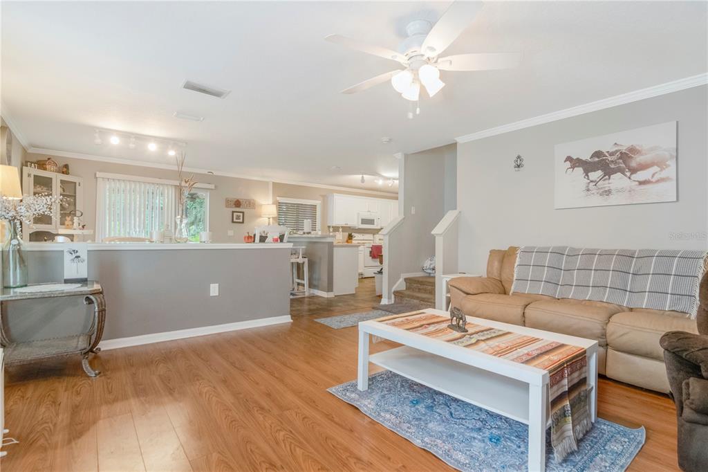 A living room with wood-look flooring, a tan sofa, and an open view into the kitchen — 19604 TIMBERBLUFF DRIVE, LAND O LAKES, FL