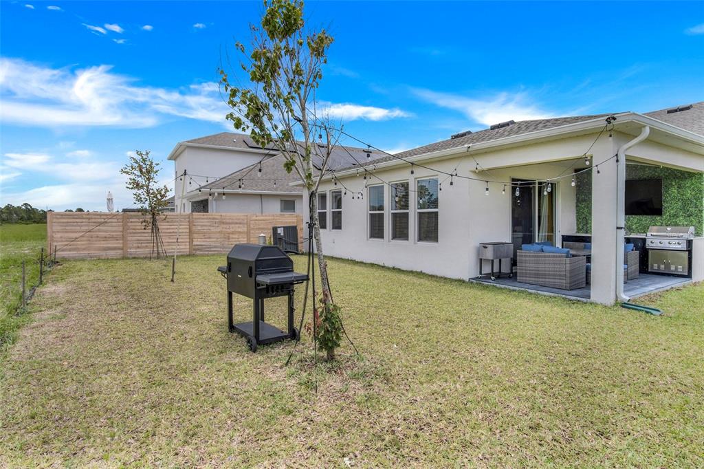 A backyard features a patio with a grill, string lights, and a wooden fence — 18863 RAWSON STREET, ORLANDO, FL
