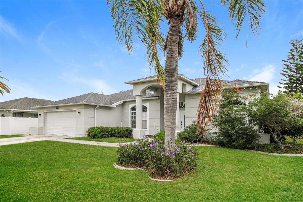 A single-story house with a white garage, a palm tree, and purple flowers in front — 4604 TRIMBLE LANE, NEW PORT RICHEY, FL