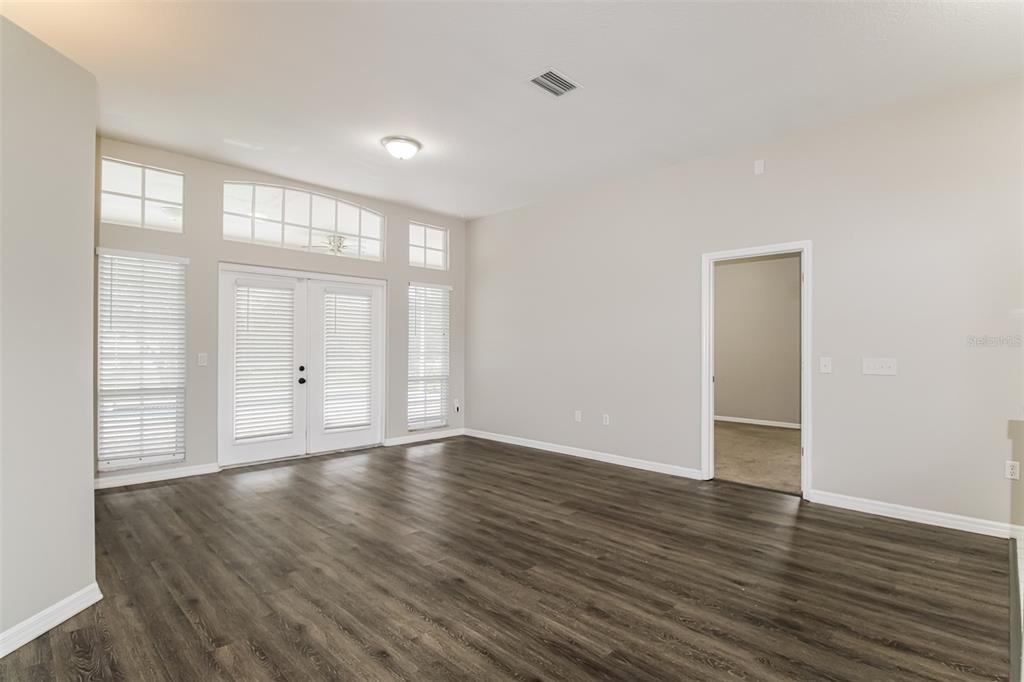 An empty room features dark wood-look flooring, light gray walls, and glass double doors — 4604 TRIMBLE LANE, NEW PORT RICHEY, FL