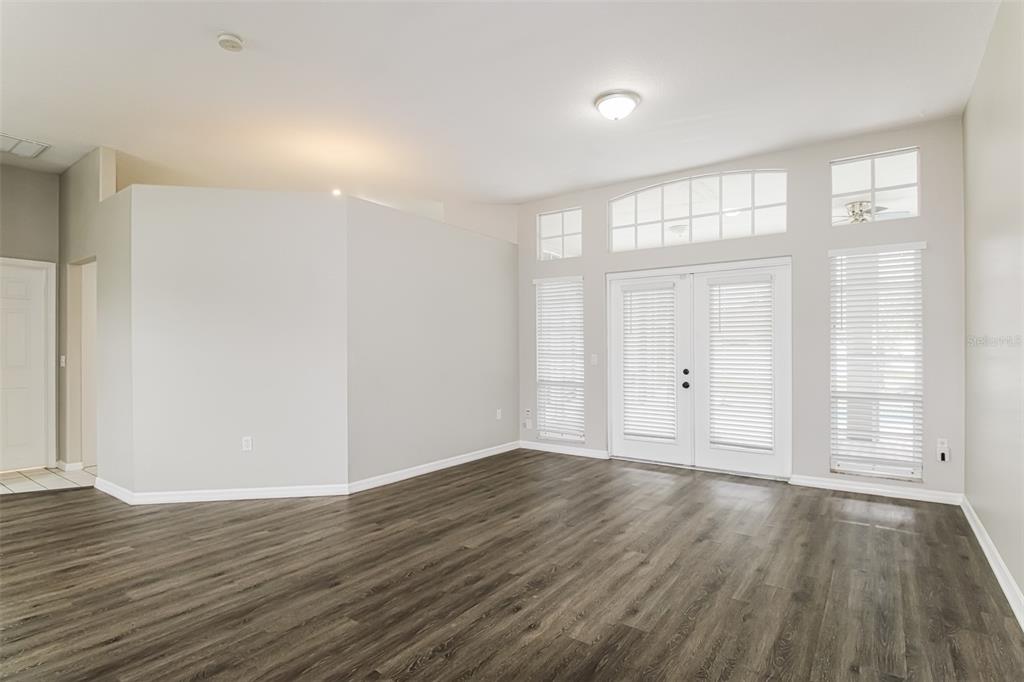 An empty living room features gray walls, dark wood-look flooring, and glass double doors — 4604 TRIMBLE LANE, NEW PORT RICHEY, FL