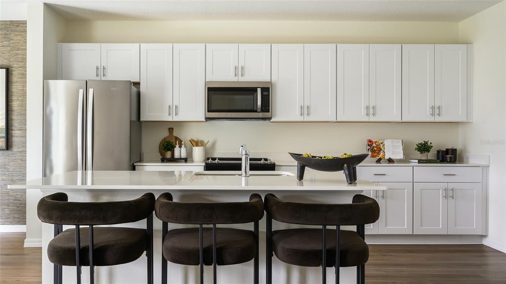 A modern kitchen features white cabinetry, stainless steel appliances, a quartz island, and dark barstools — 5444 SAN PIETRO DRIVE, WINTER HAVEN, FL