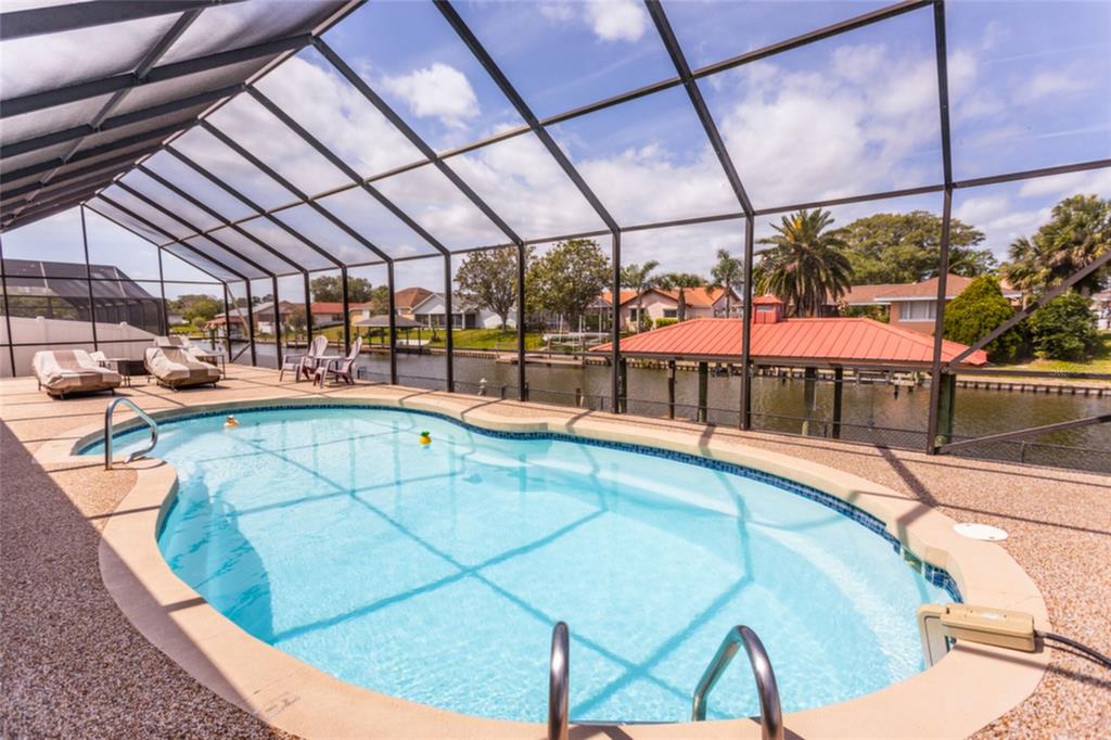 A screened-in swimming pool with a patio overlooking a canal and neighboring houses — 18 CLASSIC COURT S, PALM COAST, FL