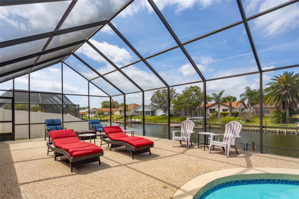 A screened-in pool deck features lounge chairs and patio seating overlooking a canal — 18 CLASSIC COURT S, PALM COAST, FL