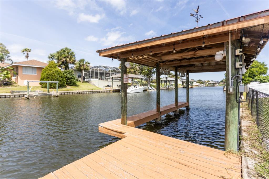 A wooden boat dock with a covered slip extends over a canal near residential homes — 18 CLASSIC COURT S, PALM COAST, FL