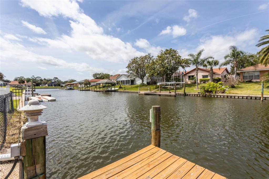 A wooden dock overlooks a canal lined with houses, boat lifts, and palm trees — 18 CLASSIC COURT S, PALM COAST, FL