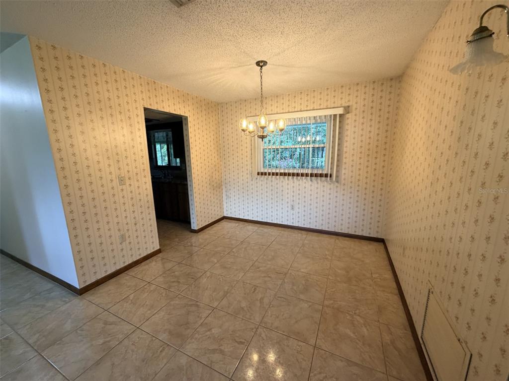 A dining room features patterned wallpaper, a chandelier, a window, and light-colored tile flooring — 9140 SW 101ST LANE, OCALA, FL
