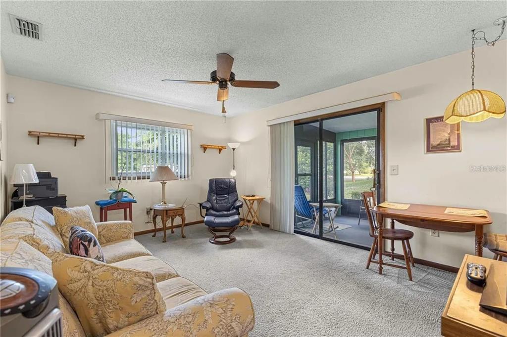 A living room with carpeted floors, a ceiling fan, a sofa, and a sliding glass door — 9140 SW 101ST LANE, OCALA, FL