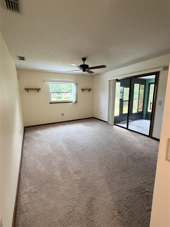 A carpeted living room features a ceiling fan, a window, and sliding glass doors — 9140 SW 101ST LANE, OCALA, FL