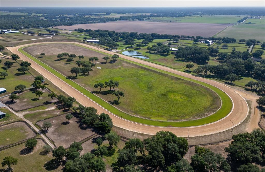 An aerial view shows a dirt horse racing track surrounded by pastures and scattered trees — 3670 SE 148TH TERRACE, MORRISTON, FL
