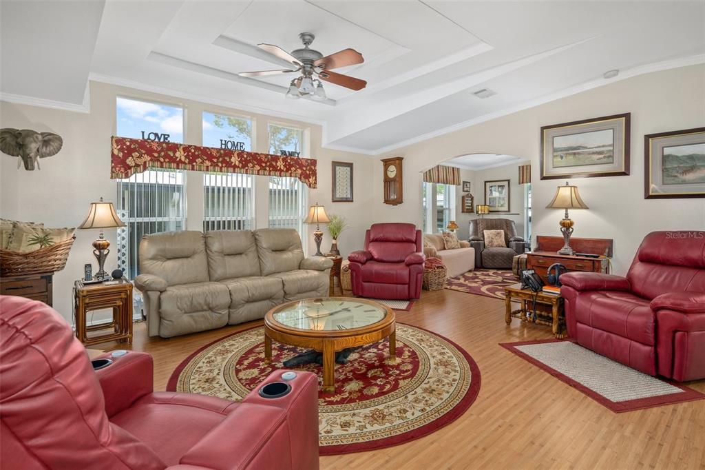 A living room features light-colored walls, wood-look flooring, a ceiling fan, and red leather furniture — 8084 LITTLE TEE LANE, BROOKSVILLE, FL