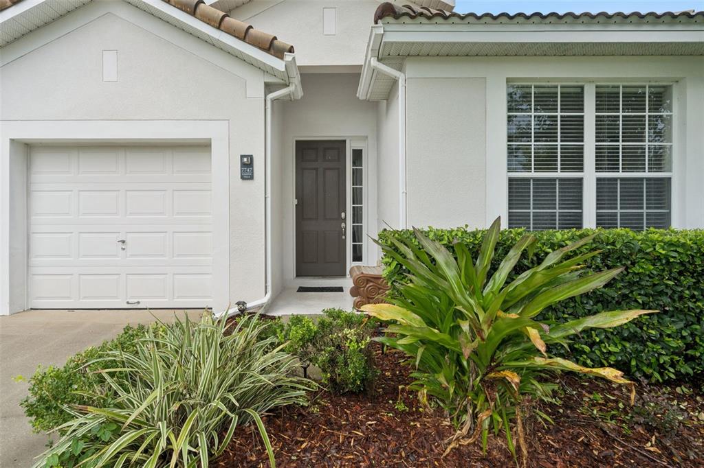 The exterior of a house features a white garage, a dark front door, and landscaping — 7747 TEASCONE BOULEVARD, KISSIMMEE, FL