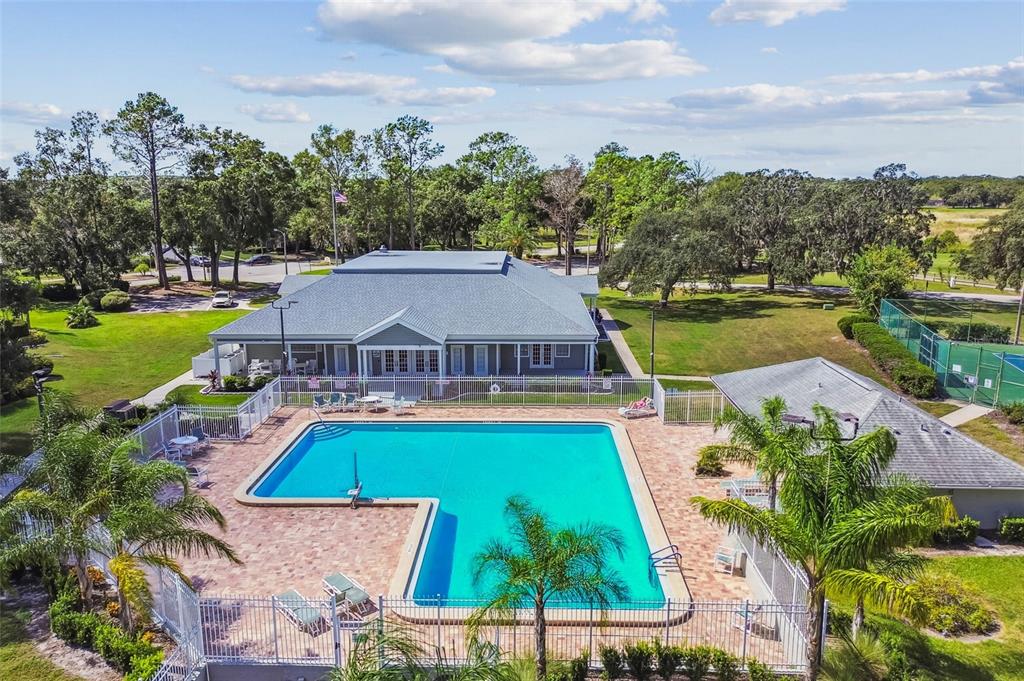 An aerial view of a community swimming pool, clubhouse, and tennis court surrounded by trees — 13816 CHESTNUT RIDGE DRIVE, HUDSON, FL