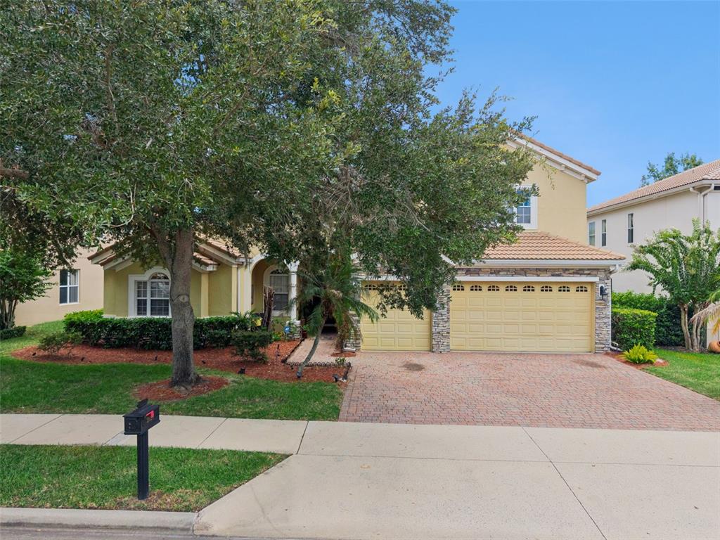 A two-story suburban house with a tan stucco exterior, stone accents, and a brick driveway — 2027 RICKOVER PLACE, WINTER GARDEN, FL