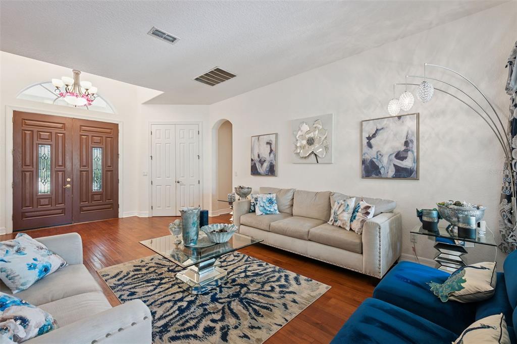 A living room features beige sofas, a glass coffee table, blue accents, and hardwood floors — 2027 RICKOVER PLACE, WINTER GARDEN, FL