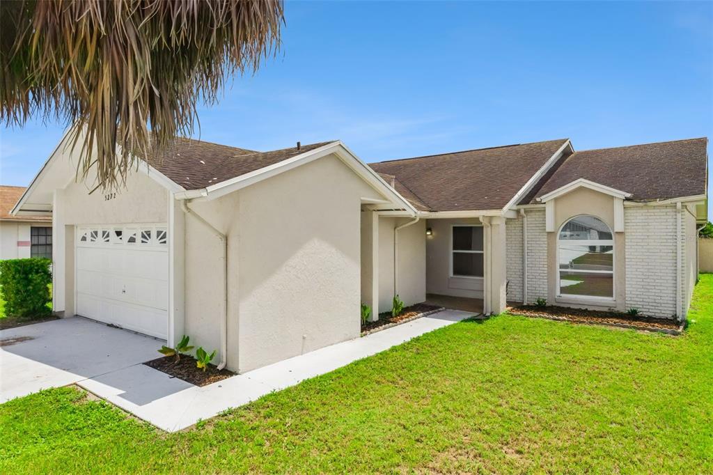 A single-story house with a white stucco and brick exterior, a garage, and a lawn — 5272 LONESOME DOVE DRIVE, KISSIMMEE, FL