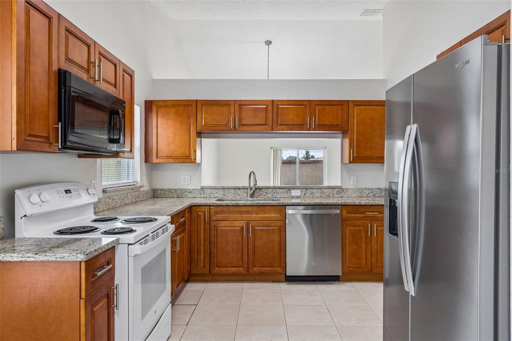 A kitchen with wood cabinets, granite countertops, stainless steel appliances, and a white stove — 5272 LONESOME DOVE DRIVE, KISSIMMEE, FL