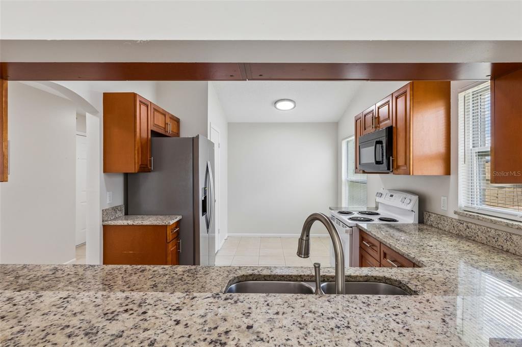 A kitchen features granite countertops, wood cabinets, stainless steel appliances, and a double basin sink — 5272 LONESOME DOVE DRIVE, KISSIMMEE, FL
