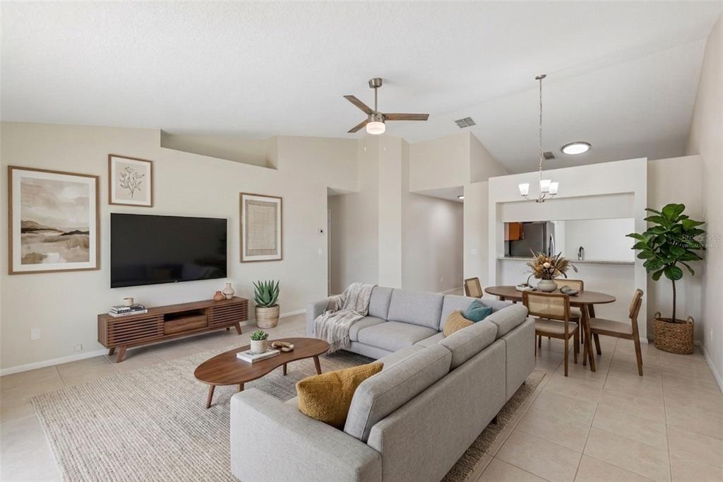 A living room with a sectional sofa, television, dining area, and neutral tile flooring — 5272 LONESOME DOVE DRIVE, KISSIMMEE, FL