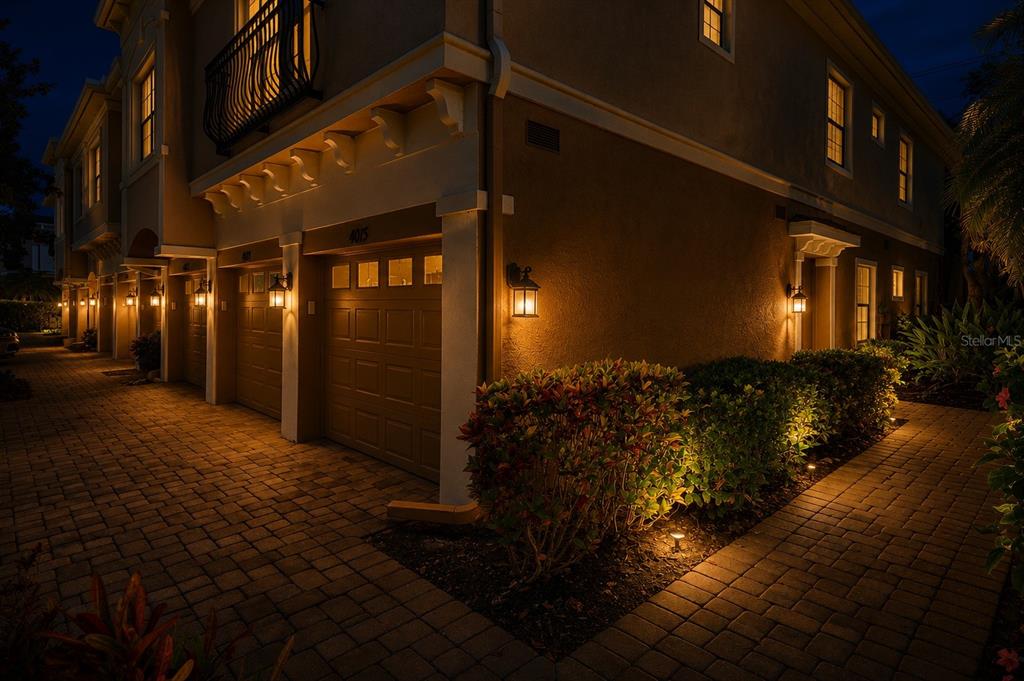 Exterior view of a multi-unit townhouse building at night with lit garage doors and landscaping — 4015 OVERTURE CIRCLE UNIT 314, BRADENTON, FL