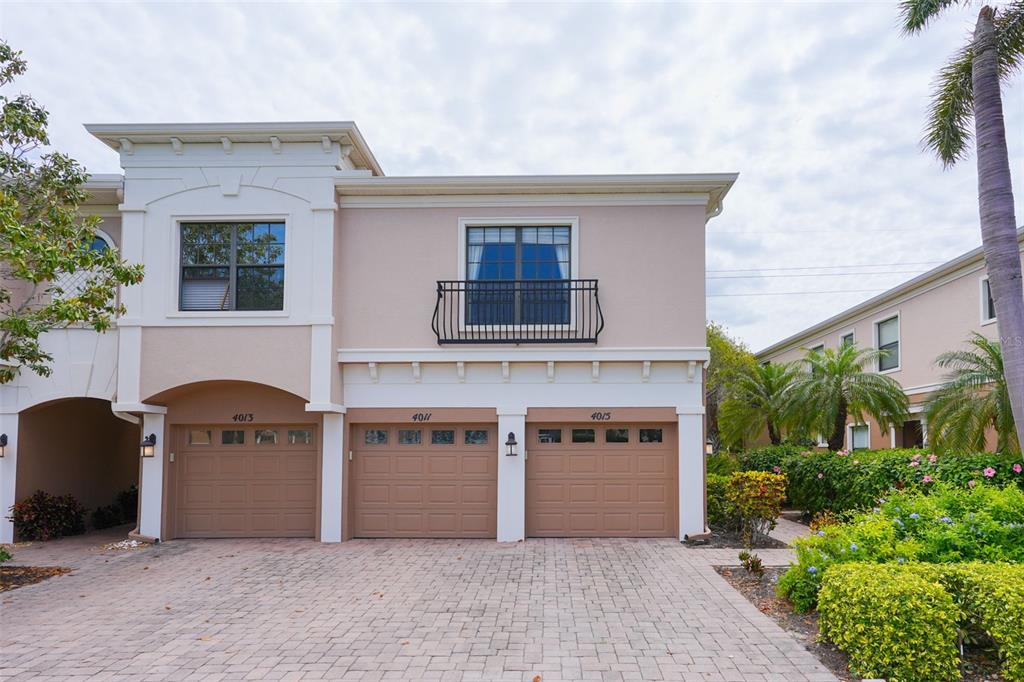 A two-story townhouse exterior features three garage doors, a balcony, and a paved driveway — 4015 OVERTURE CIRCLE UNIT 314, BRADENTON, FL