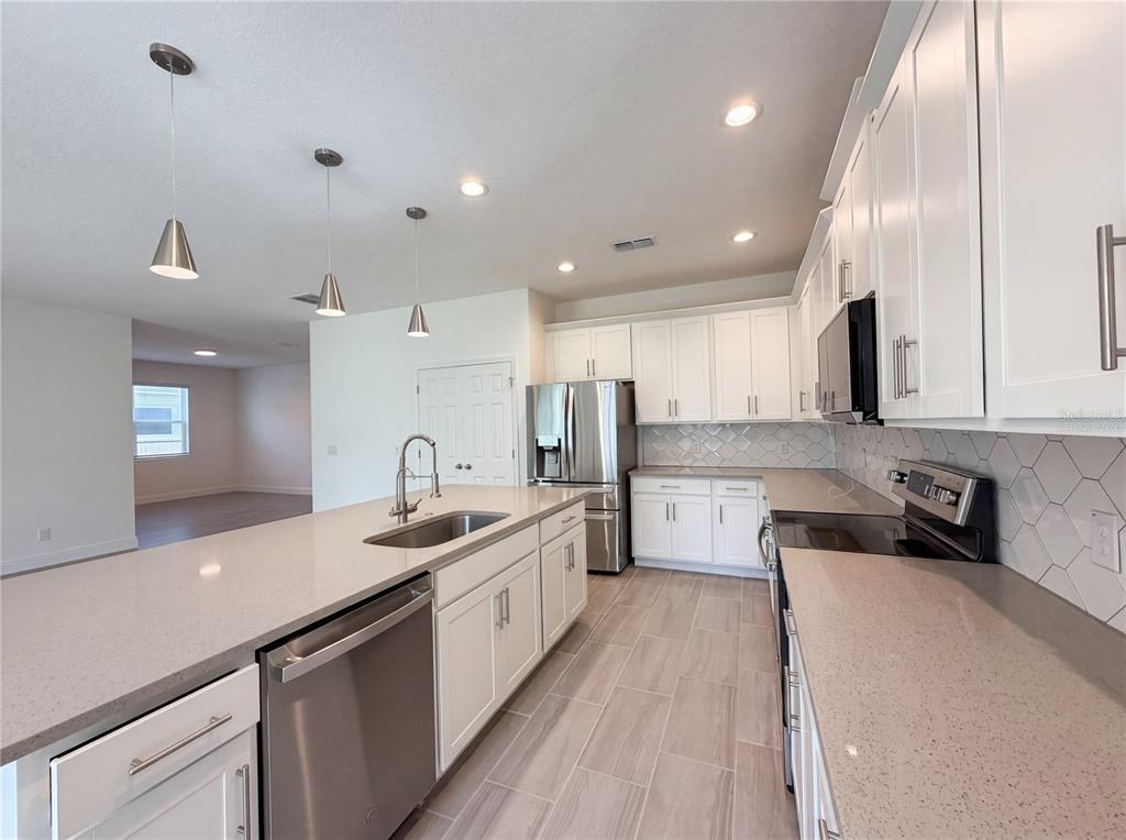 A modern kitchen features white cabinets, quartz countertops, stainless steel appliances, and a large island — 7725 SCICLI WAY, CLERMONT, FL
