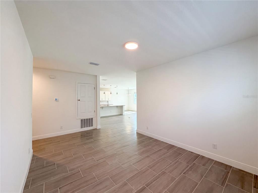 A room with light-colored walls and wood-look tile flooring leads into an open kitchen — 7725 SCICLI WAY, CLERMONT, FL