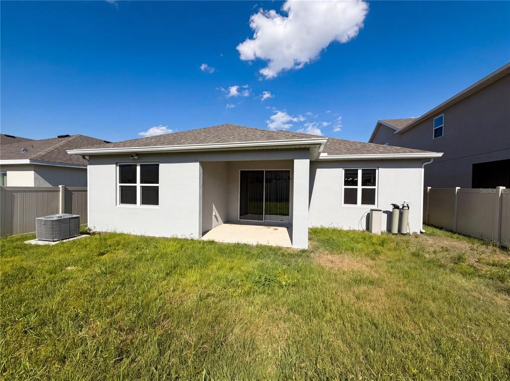 The exterior rear view of a single-story house features a concrete patio and fenced yard — 7725 SCICLI WAY, CLERMONT, FL