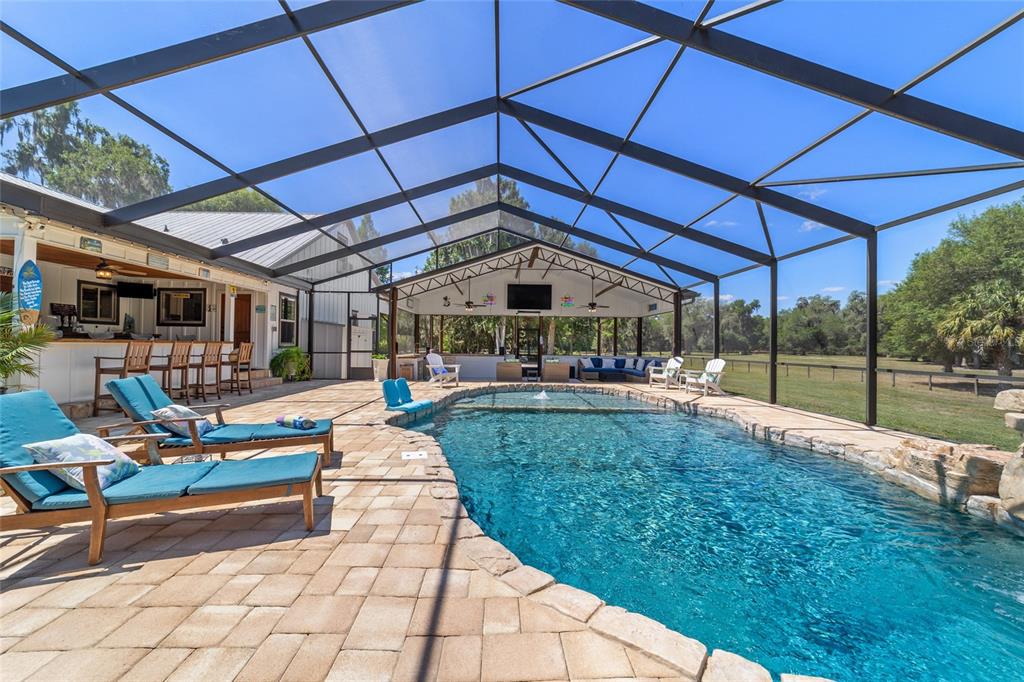 A screened-in pool area features a stone-edged swimming pool, lounge chairs, and an outdoor bar — 20005 NW 135TH AVENUE, MICANOPY, FL