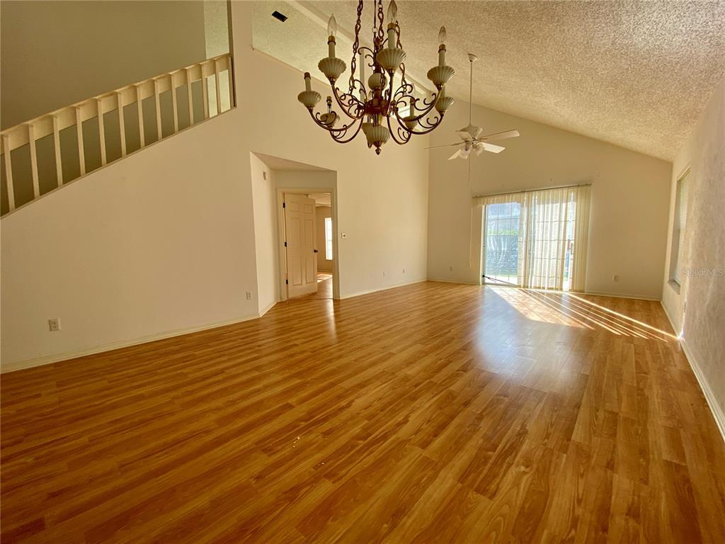 A living room with wood-look flooring, a vaulted ceiling, a chandelier, and a staircase — 101 BRAEBURN CIRCLE, DAYTONA BEACH, FL