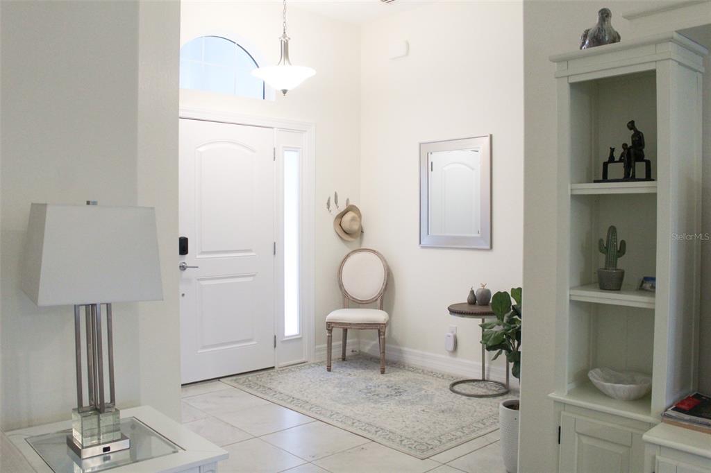 A bright entryway features a white front door, a patterned area rug, and a tall bookshelf — 206 ANTILLA DRIVE, ROTONDA WEST, FL