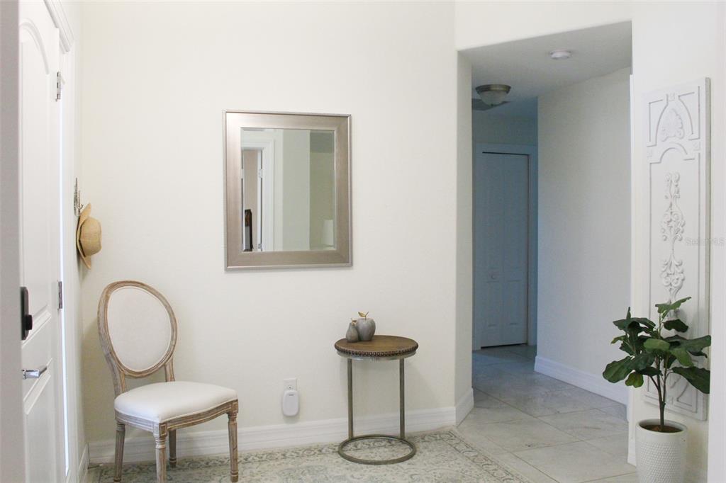 A bright entryway features a white chair, a small side table, a mirror, and a plant — 206 ANTILLA DRIVE, ROTONDA WEST, FL