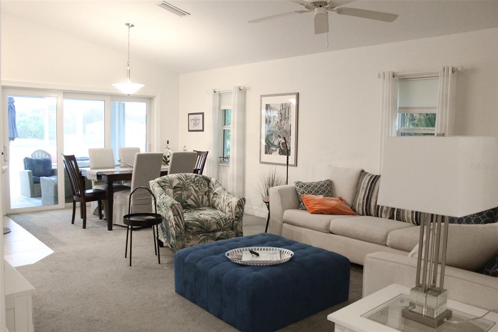 A living and dining room with carpeted floors, a blue ottoman, and a sliding glass door — 206 ANTILLA DRIVE, ROTONDA WEST, FL