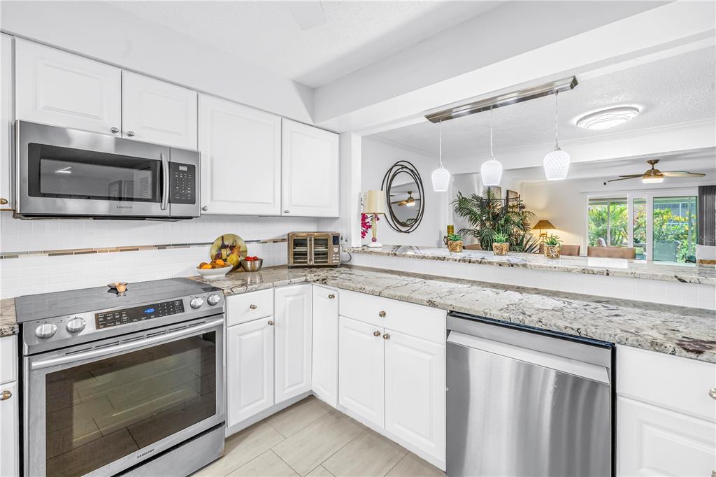 A kitchen with white cabinets, stainless steel appliances, and granite countertops overlooks a living area — 3465 41ST TERRACE S UNIT 205, ST PETERSBURG, FL