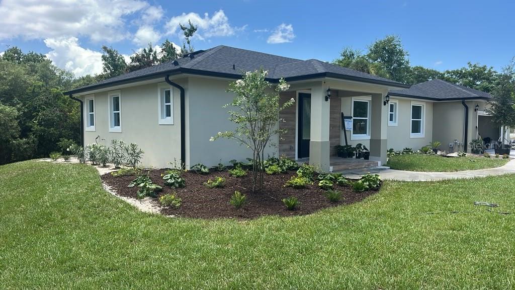 A single-story house with light-colored stucco walls, a dark shingled roof, and landscaped front yard — 4880 BARNA AVENUE, TITUSVILLE, FL