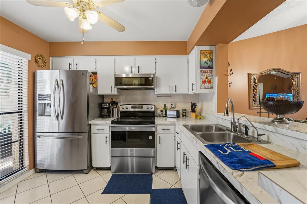 A kitchen features white cabinetry, stainless steel appliances, and marble-look countertops with orange walls — 317 KNOTTWOOD COURT UNIT 317, SUN CITY CENTER, FL