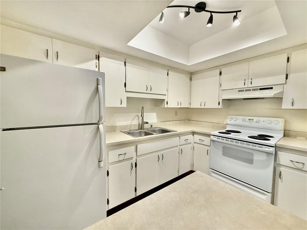 A kitchen features white cabinets, a white stove, and a countertop with a pass-through window — 2217 HOPKINS DRIVE W UNIT 2217, BRADENTON, FL