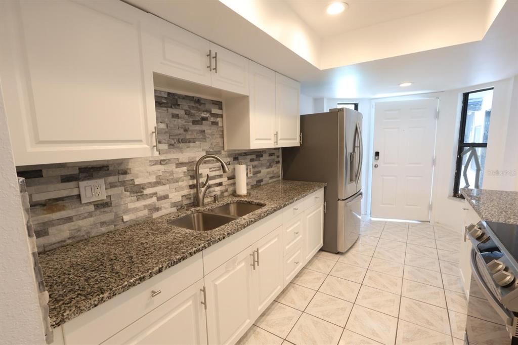 A kitchen features white cabinets, granite countertops, a stone backsplash, and stainless steel appliances — 1649 PENDLETON STREET, DELTONA, FL