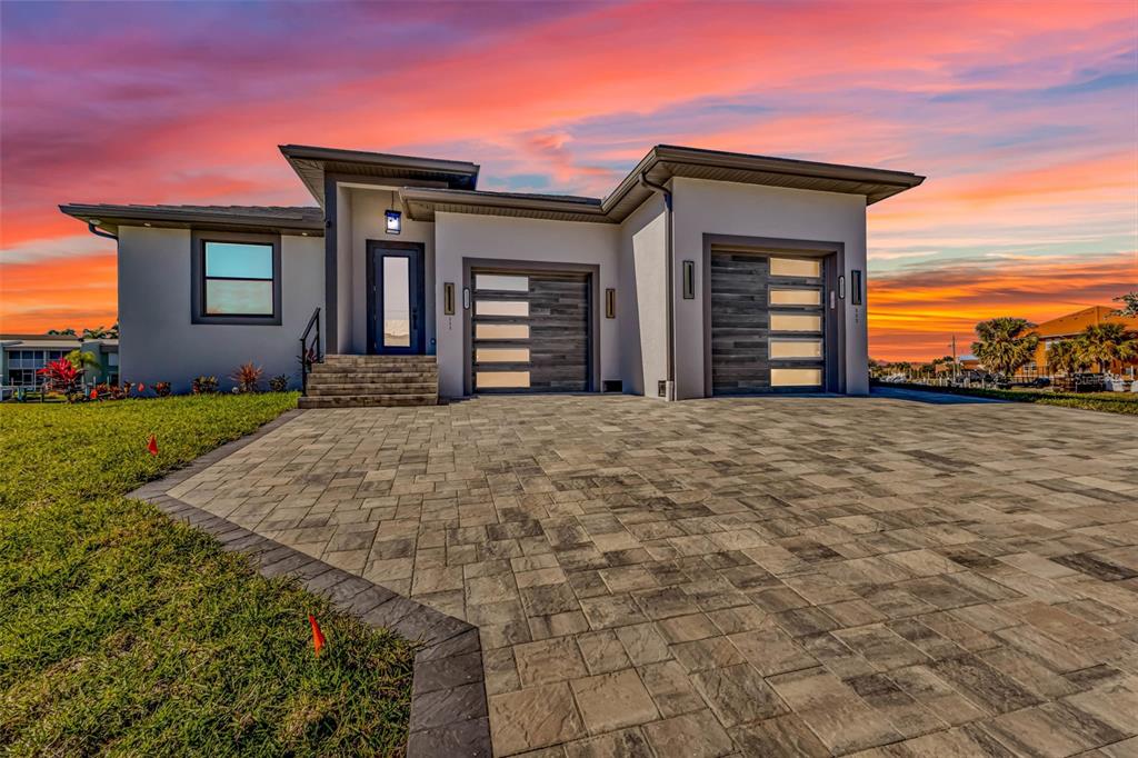 A modern single-story house with a paved driveway, two garage doors, and a sunset sky — 1323 WESLEY DRIVE UNIT 112, PUNTA GORDA, FL
