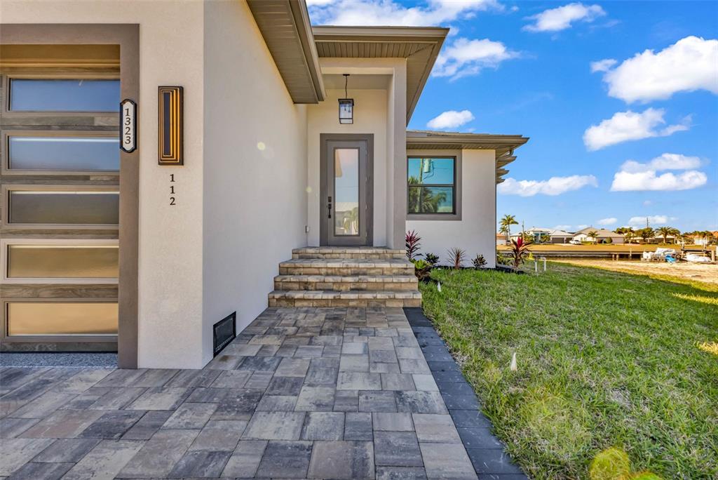 A modern house exterior features a paved walkway, stone steps, and a glass-paneled front door — 1323 WESLEY DRIVE UNIT 112, PUNTA GORDA, FL