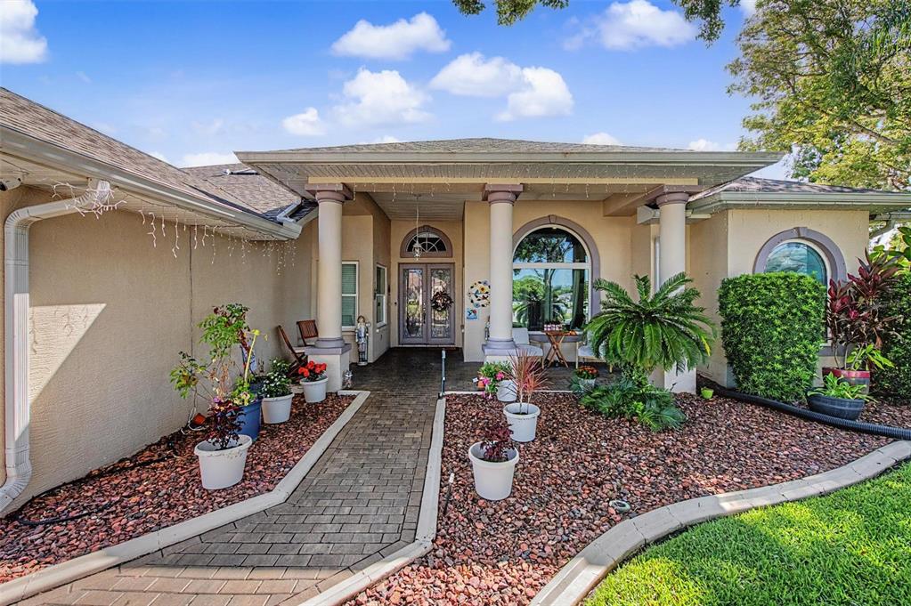 A paved walkway leads to the covered entrance of a house with beige stucco walls — 8835 HELMSLY LANE, HUDSON, FL