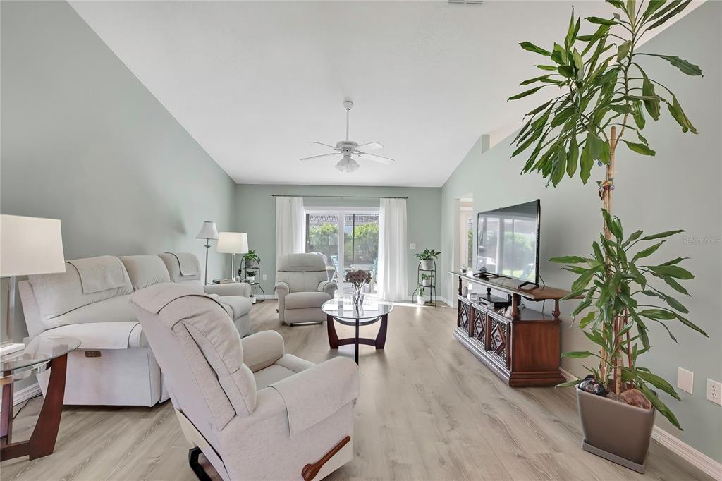 A living room features light-colored walls, wood-look flooring, a ceiling fan, and a sliding glass door — 7274 ALOE DRIVE, SPRING HILL, FL